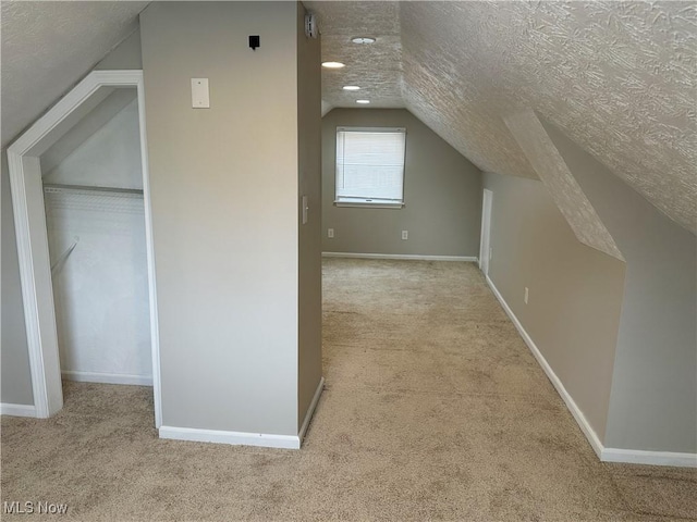 additional living space featuring a textured ceiling, light colored carpet, and lofted ceiling