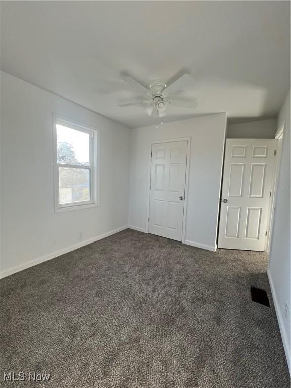 unfurnished bedroom with ceiling fan and dark colored carpet