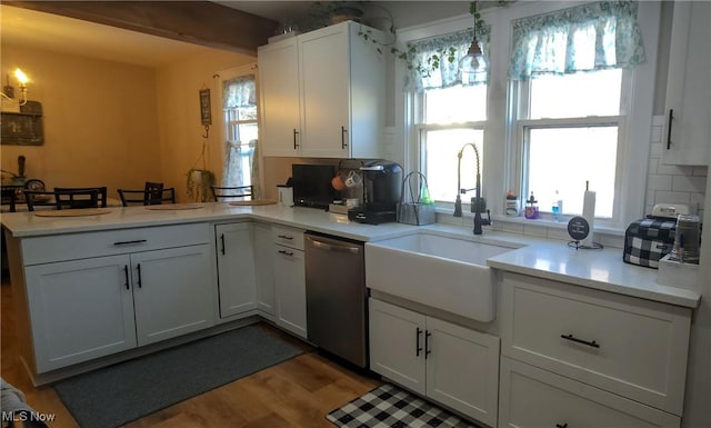 kitchen with light countertops, white cabinets, a sink, dishwasher, and a peninsula