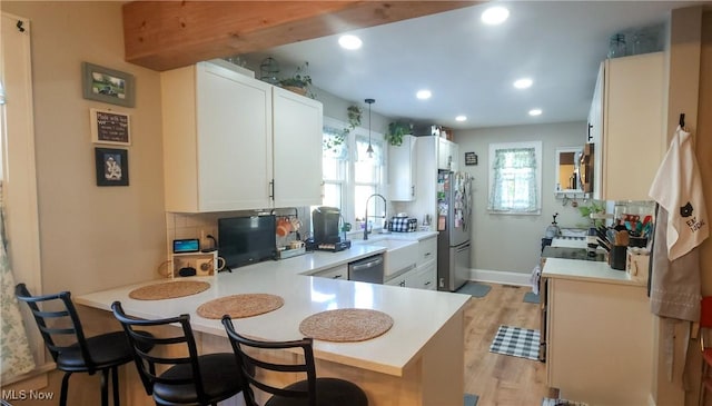 kitchen with a kitchen breakfast bar, a peninsula, stainless steel appliances, light countertops, and a sink