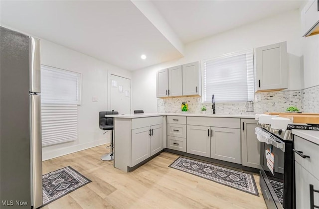 kitchen featuring sink, decorative backsplash, appliances with stainless steel finishes, light hardwood / wood-style floors, and kitchen peninsula