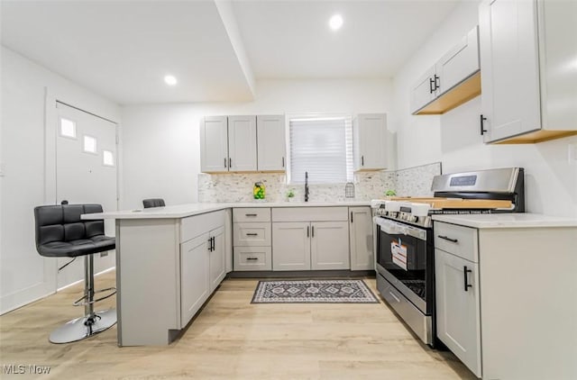 kitchen featuring a kitchen bar, kitchen peninsula, stainless steel range, sink, and light hardwood / wood-style floors