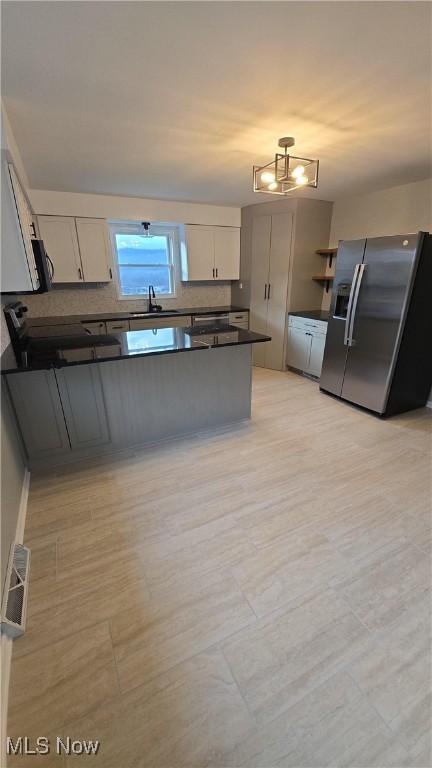 kitchen with sink, hanging light fixtures, stainless steel fridge with ice dispenser, backsplash, and kitchen peninsula