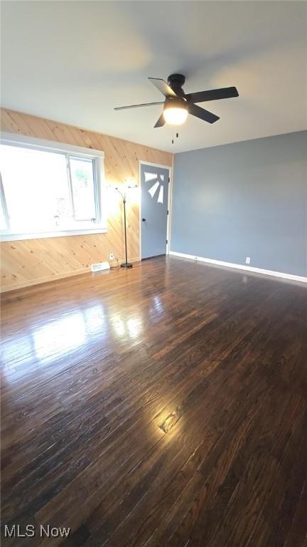 empty room featuring wooden walls, dark hardwood / wood-style flooring, and ceiling fan