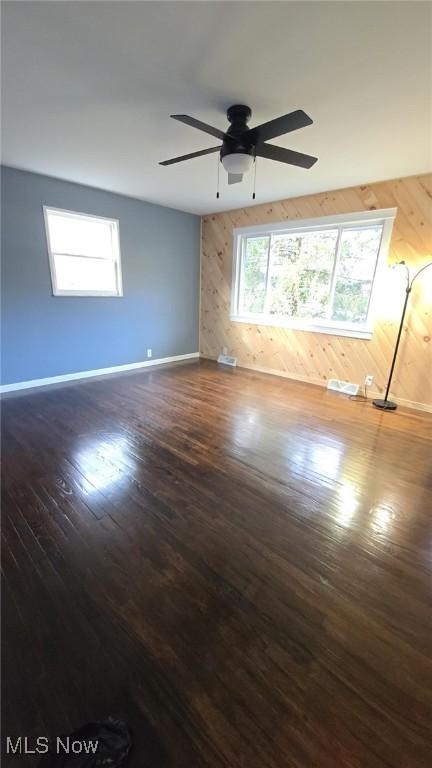 spare room with ceiling fan, wood walls, and dark hardwood / wood-style flooring