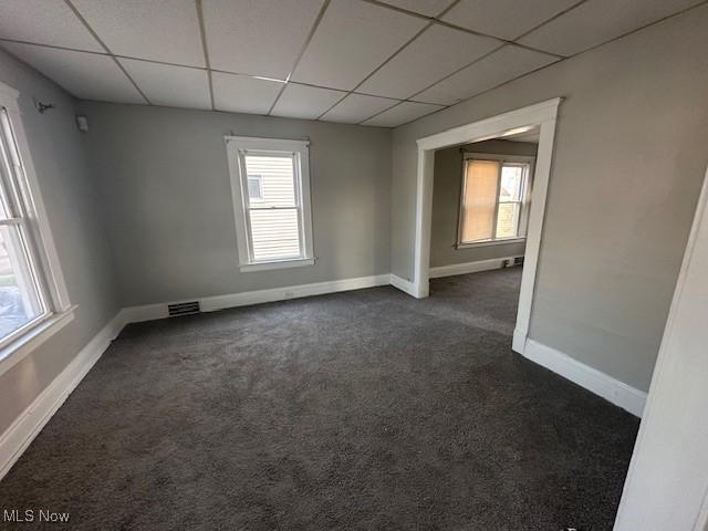 carpeted empty room with plenty of natural light and a drop ceiling