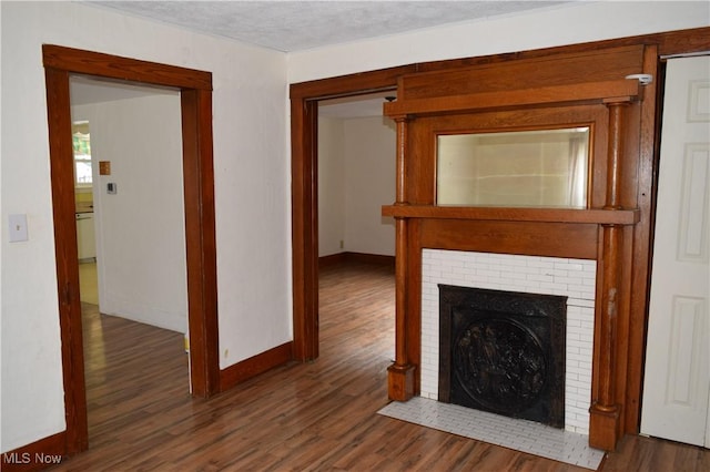 unfurnished living room with dark wood-type flooring, a textured ceiling, and a brick fireplace