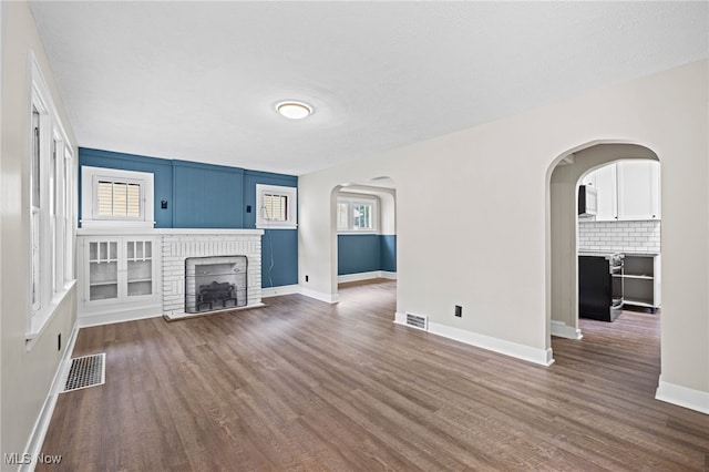 unfurnished living room featuring a brick fireplace and dark wood-type flooring