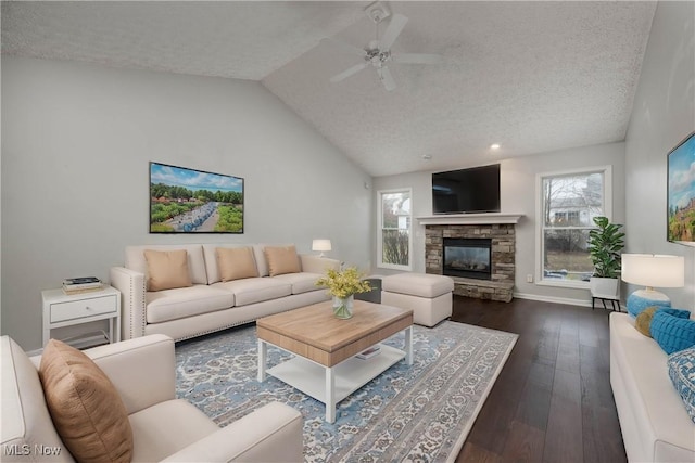 living room with dark wood-type flooring, vaulted ceiling, ceiling fan, a textured ceiling, and a fireplace