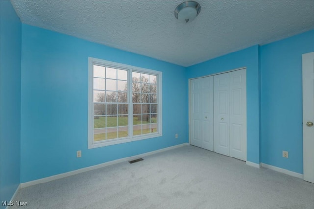 unfurnished bedroom featuring light colored carpet, a textured ceiling, and a closet