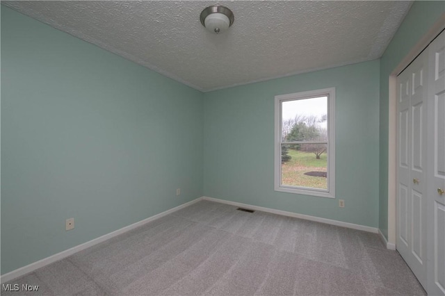 unfurnished bedroom with light colored carpet, a textured ceiling, and a closet