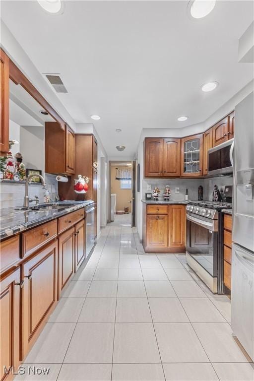 kitchen with sink, backsplash, dark stone countertops, light tile patterned floors, and appliances with stainless steel finishes