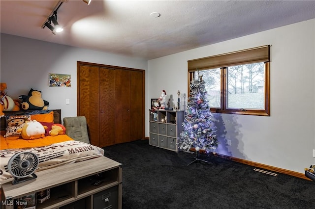 carpeted bedroom with a textured ceiling, rail lighting, and a closet