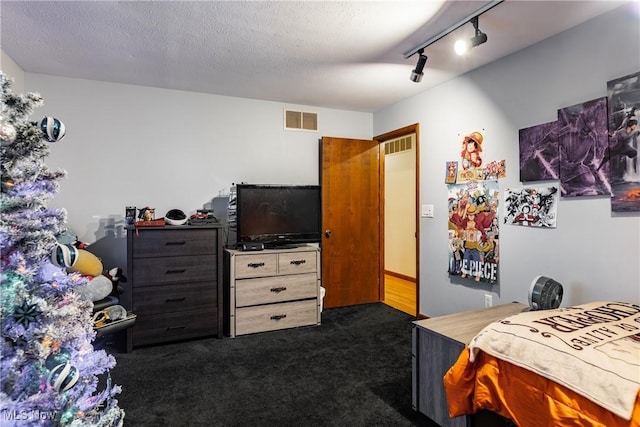 bedroom featuring track lighting, dark carpet, and a textured ceiling