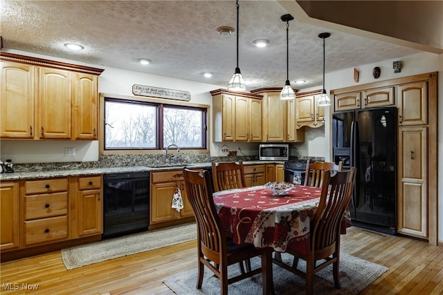 kitchen featuring light stone counters, pendant lighting, black appliances, and light hardwood / wood-style flooring