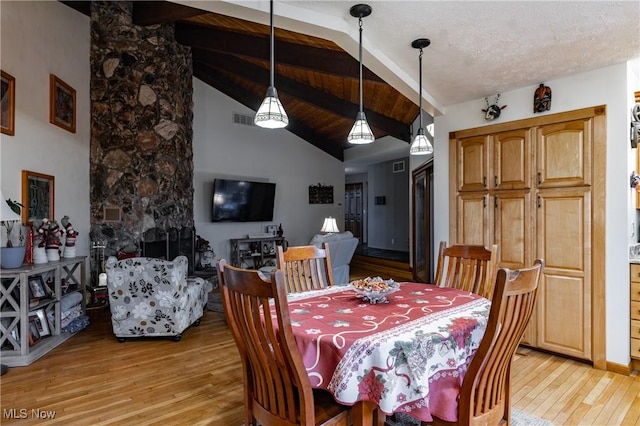 dining room with vaulted ceiling with beams, a stone fireplace, and light hardwood / wood-style floors