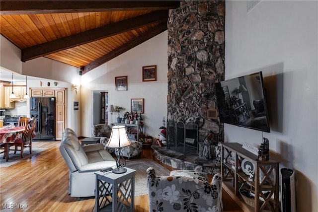 living room featuring beam ceiling, high vaulted ceiling, light hardwood / wood-style flooring, wooden ceiling, and a stone fireplace