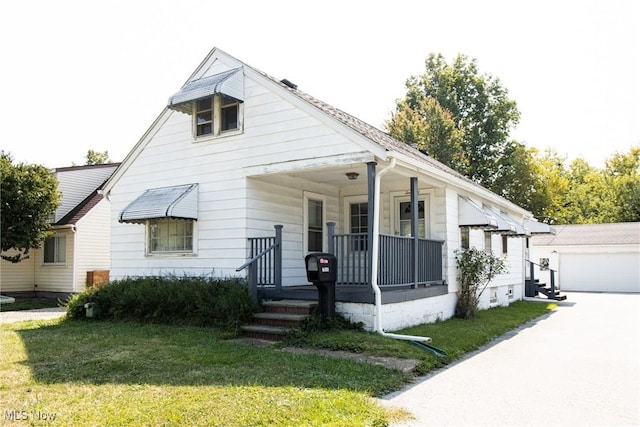 view of front of home with an outdoor structure, covered porch, a front yard, and a garage