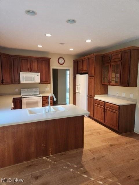 kitchen with kitchen peninsula, sink, light hardwood / wood-style floors, and white appliances