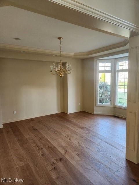 unfurnished dining area with hardwood / wood-style floors, crown molding, and a notable chandelier