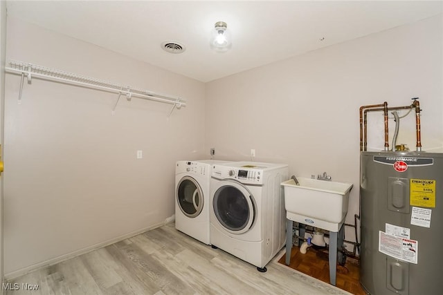 clothes washing area with washer and dryer, light wood-type flooring, sink, and water heater