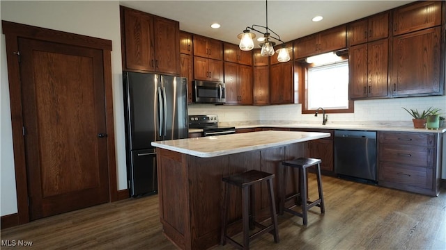 kitchen with decorative backsplash, stainless steel appliances, dark wood-type flooring, a center island, and hanging light fixtures