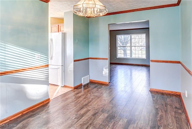 unfurnished room with a textured ceiling, a notable chandelier, wood-type flooring, and ornamental molding