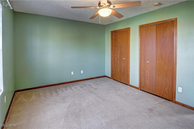 unfurnished bedroom with multiple closets, ceiling fan, light colored carpet, and a textured ceiling