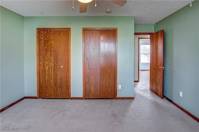 unfurnished bedroom featuring a textured ceiling, light colored carpet, and two closets