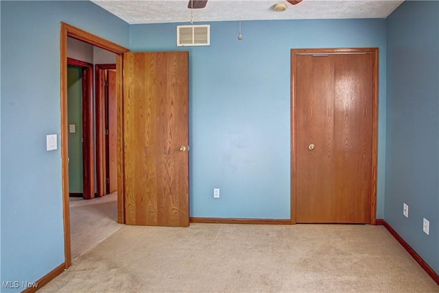 unfurnished bedroom with light carpet, ceiling fan, and a textured ceiling