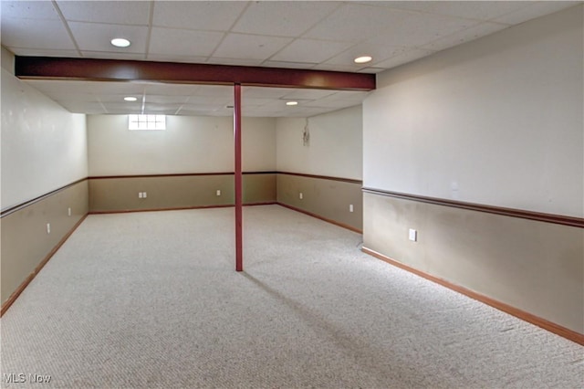 basement with a paneled ceiling and light colored carpet