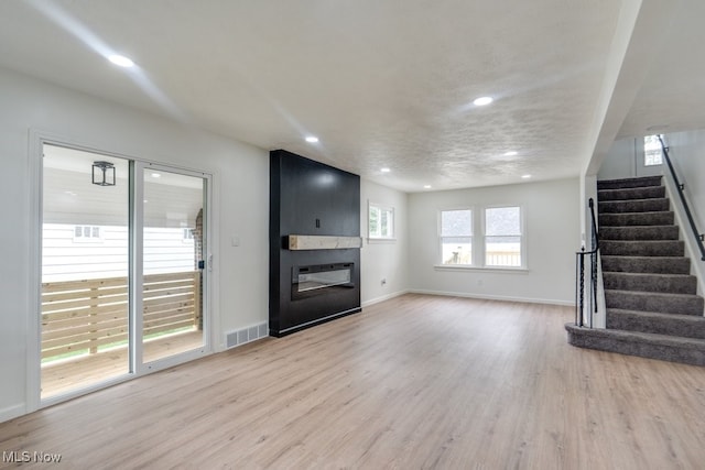 unfurnished living room with a fireplace, a textured ceiling, and light hardwood / wood-style flooring