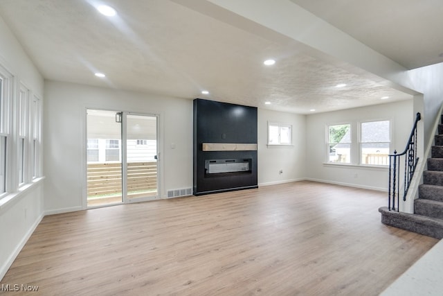 unfurnished living room featuring a large fireplace, light hardwood / wood-style flooring, and a textured ceiling