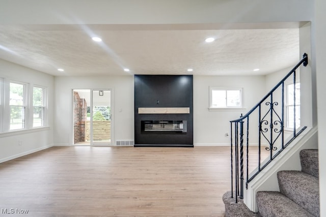 unfurnished living room featuring a large fireplace, light hardwood / wood-style floors, and a textured ceiling