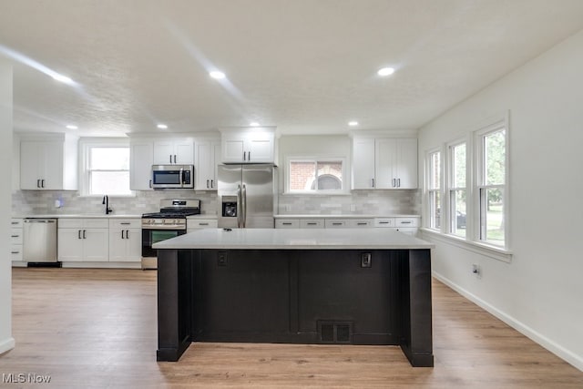 kitchen with a healthy amount of sunlight, a kitchen island, white cabinetry, and stainless steel appliances