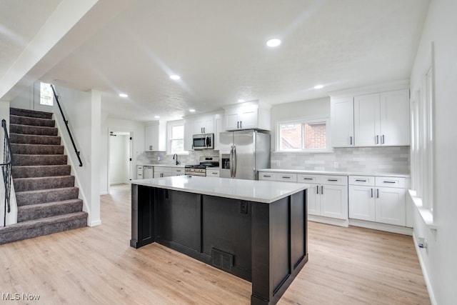 kitchen featuring a center island, stainless steel appliances, backsplash, light hardwood / wood-style floors, and white cabinets