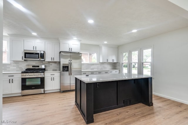 kitchen featuring backsplash, light wood-type flooring, appliances with stainless steel finishes, a kitchen island, and white cabinetry