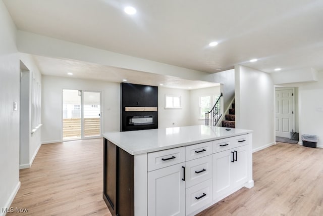 kitchen featuring light wood-type flooring, a center island, white cabinetry, and light stone counters