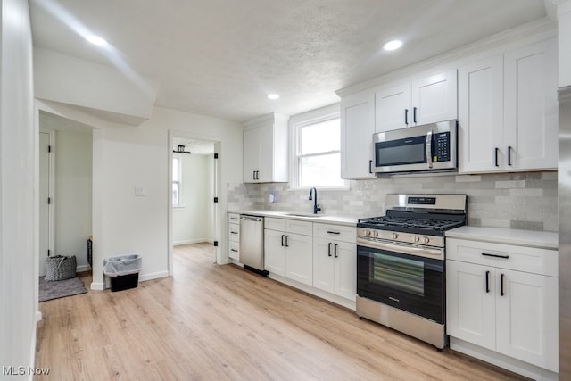 kitchen with decorative backsplash, stainless steel appliances, sink, white cabinets, and light hardwood / wood-style floors