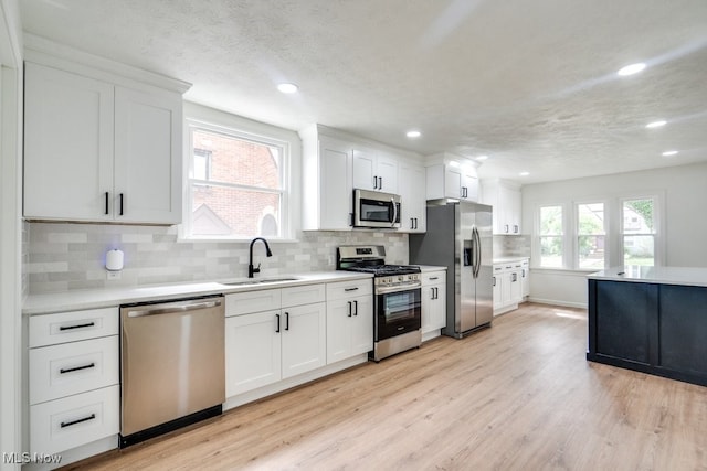 kitchen with white cabinetry, sink, tasteful backsplash, light hardwood / wood-style floors, and appliances with stainless steel finishes