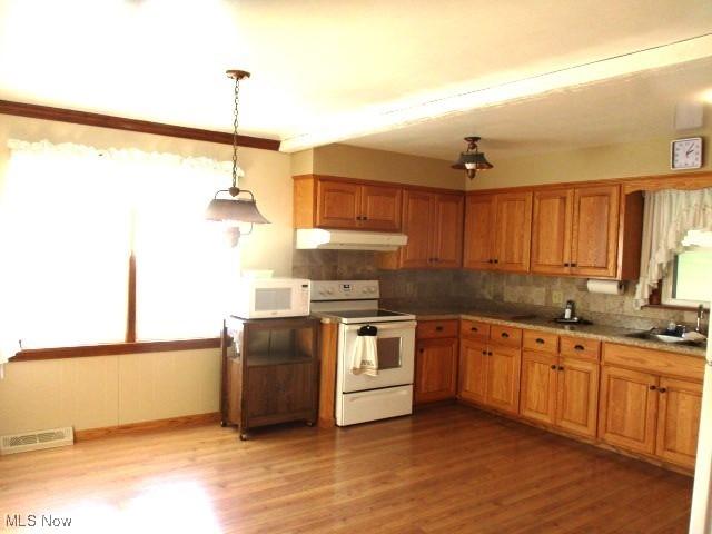 kitchen with backsplash, pendant lighting, white appliances, and light wood-type flooring