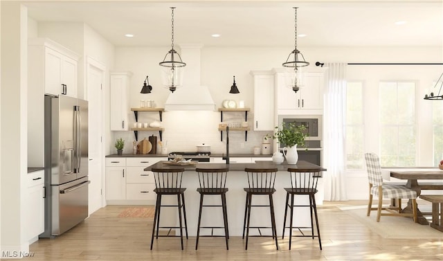 kitchen featuring stainless steel appliances, an island with sink, pendant lighting, light hardwood / wood-style floors, and white cabinets