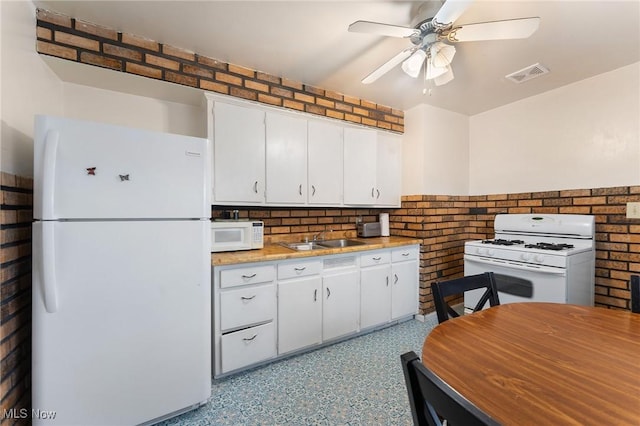 kitchen with brick wall, white appliances, ceiling fan, sink, and white cabinets