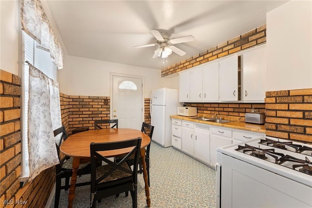 kitchen featuring white appliances, sink, ceiling fan, white cabinetry, and brick wall