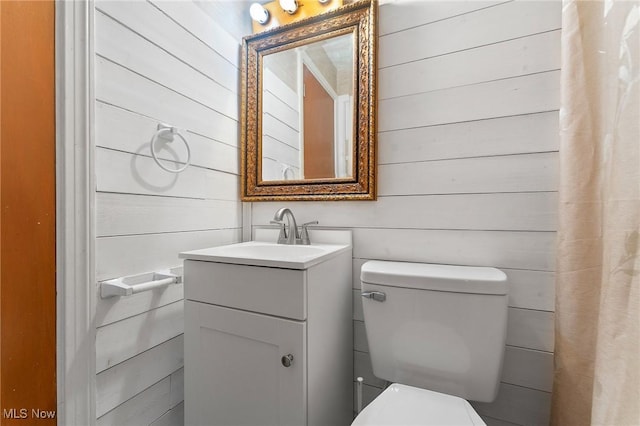 bathroom featuring vanity, wood walls, and toilet