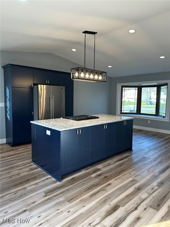 kitchen with stainless steel refrigerator, a large island with sink, pendant lighting, vaulted ceiling, and light wood-type flooring