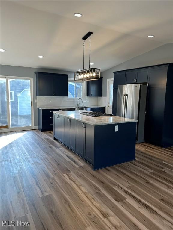 kitchen featuring stainless steel appliances, hardwood / wood-style floors, a kitchen island, hanging light fixtures, and lofted ceiling