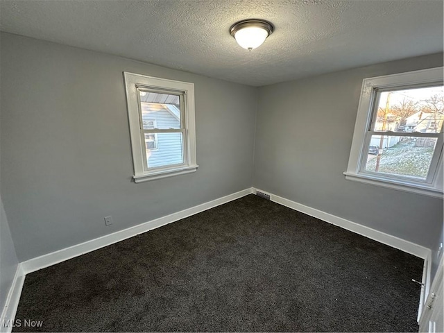 unfurnished room featuring dark carpet and a textured ceiling