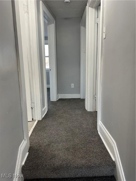 corridor featuring dark colored carpet and a textured ceiling