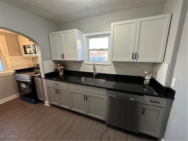 kitchen with tasteful backsplash, stainless steel appliances, dark wood-type flooring, sink, and white cabinetry